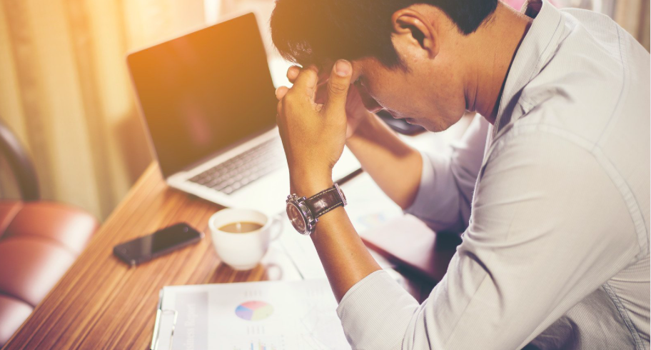 Man sitting at desk with laptop, holding head in hands showing work stress