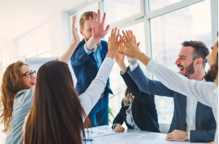 Business team giving high fives across a conference table in a bright office