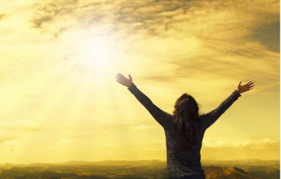 Silhouette of a person with arms outstretched toward golden sunrise sky, symbolizing hope and overcoming adversity.
