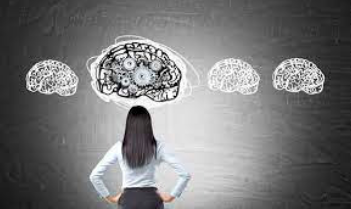 Rear view of a woman with hands on hips looking at chalk-drawn brain illustrations on a dark wall, one with gears inside