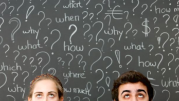 Two children looking up at a blackboard covered with question marks and words like why, what, how, when