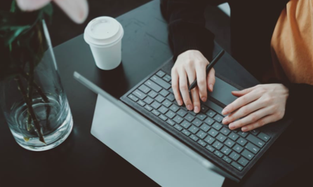 Hands typing on a laptop keyboard with a coffee cup nearby, suggesting overwork and stress