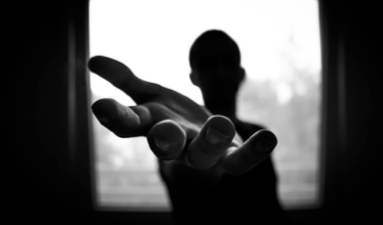 Silhouette of a person with outstretched hand reaching toward bright window light, suggesting hope or seeking help