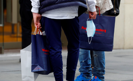 Two people holding shopping bags, one with a face mask dangling from their hand