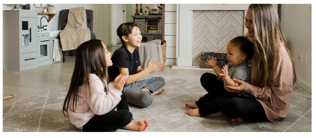 A mother sitting on the floor playing with three young children in a cozy living room
