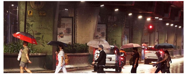 Several people walking on a city street at night holding umbrellas during heavy rainfall, with cars and traffic lights