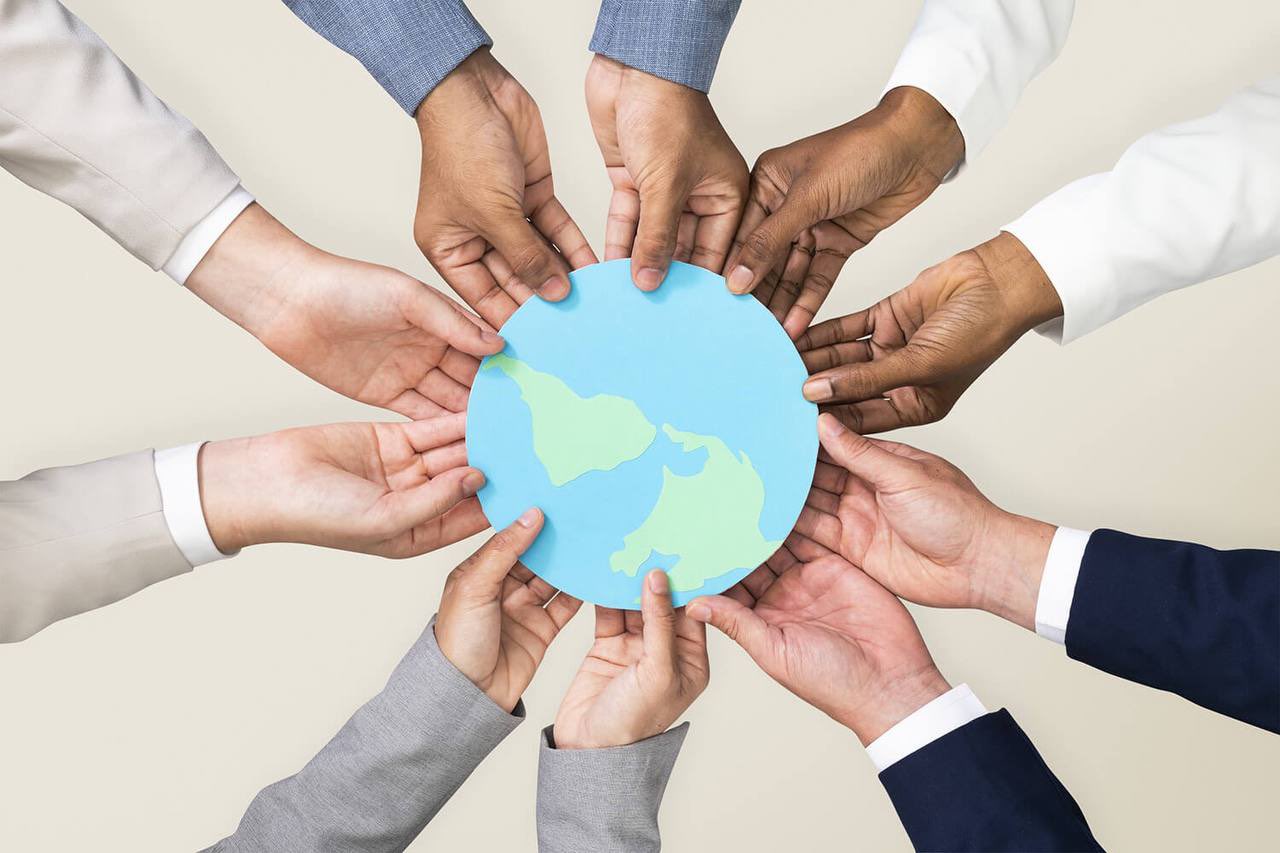 Multiple diverse hands in business attire jointly holding a small paper globe, symbolizing global cooperation and shared