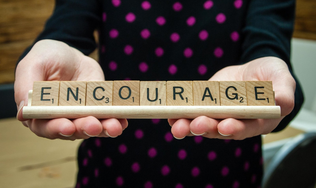 Two hands hold wooden letter blocks spelling the word encourage